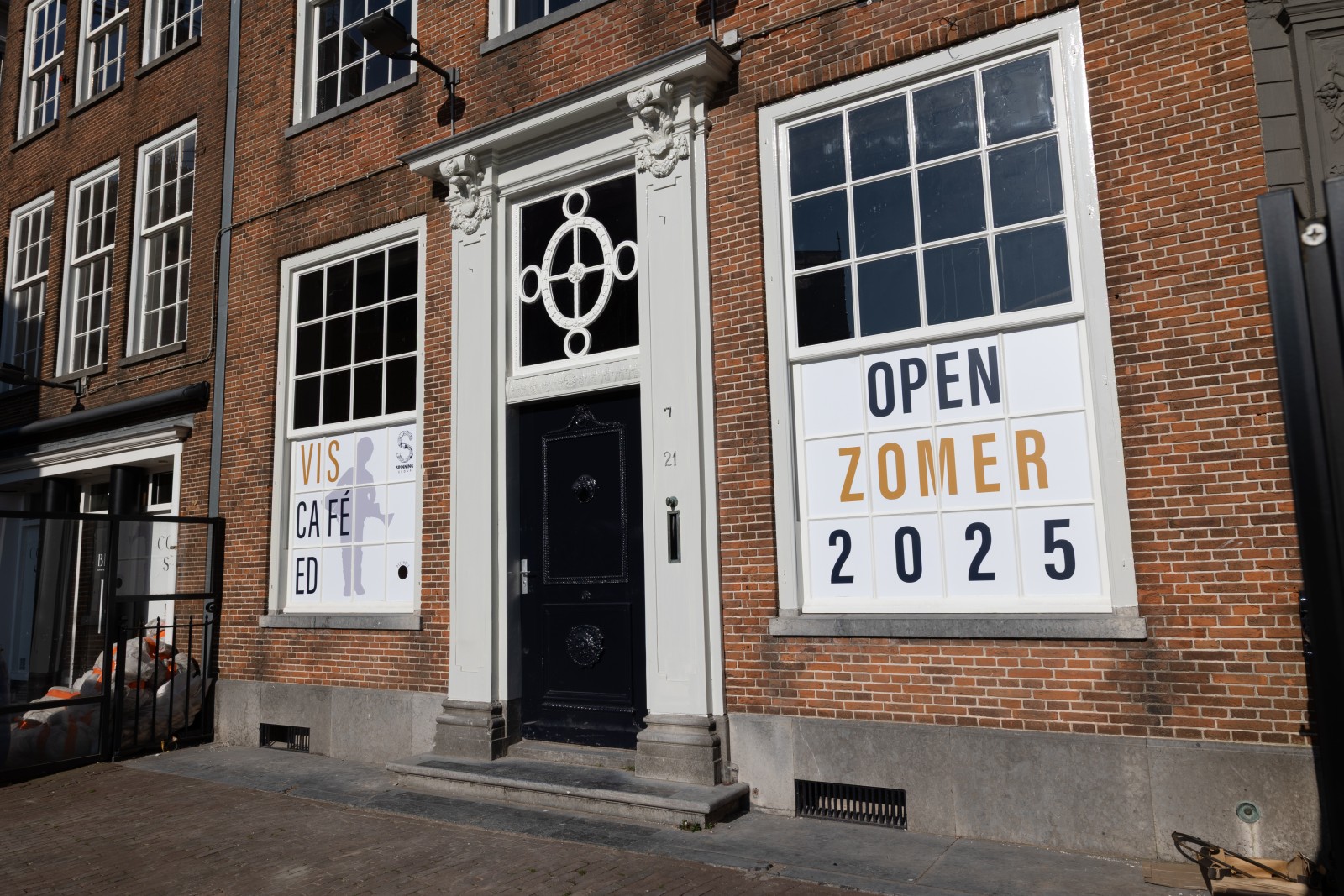 Gevel van historisch pand met grote ramen. Borden kondigen opening viscafé zomer 2025 aan.