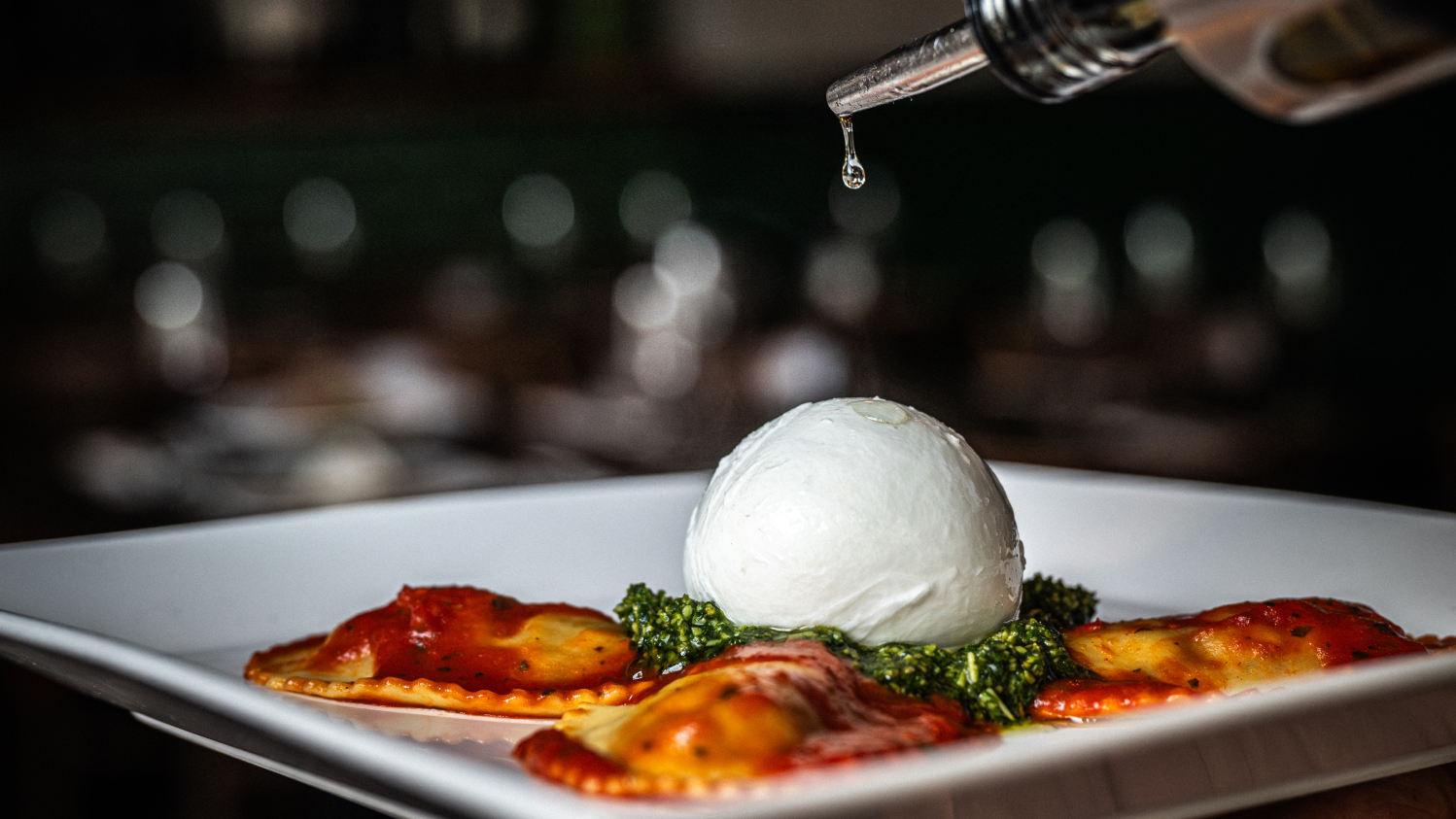 Creamy burrata with vibrant pesto, surrounded by tomato-sauced ravioli, drizzled with olive oil.