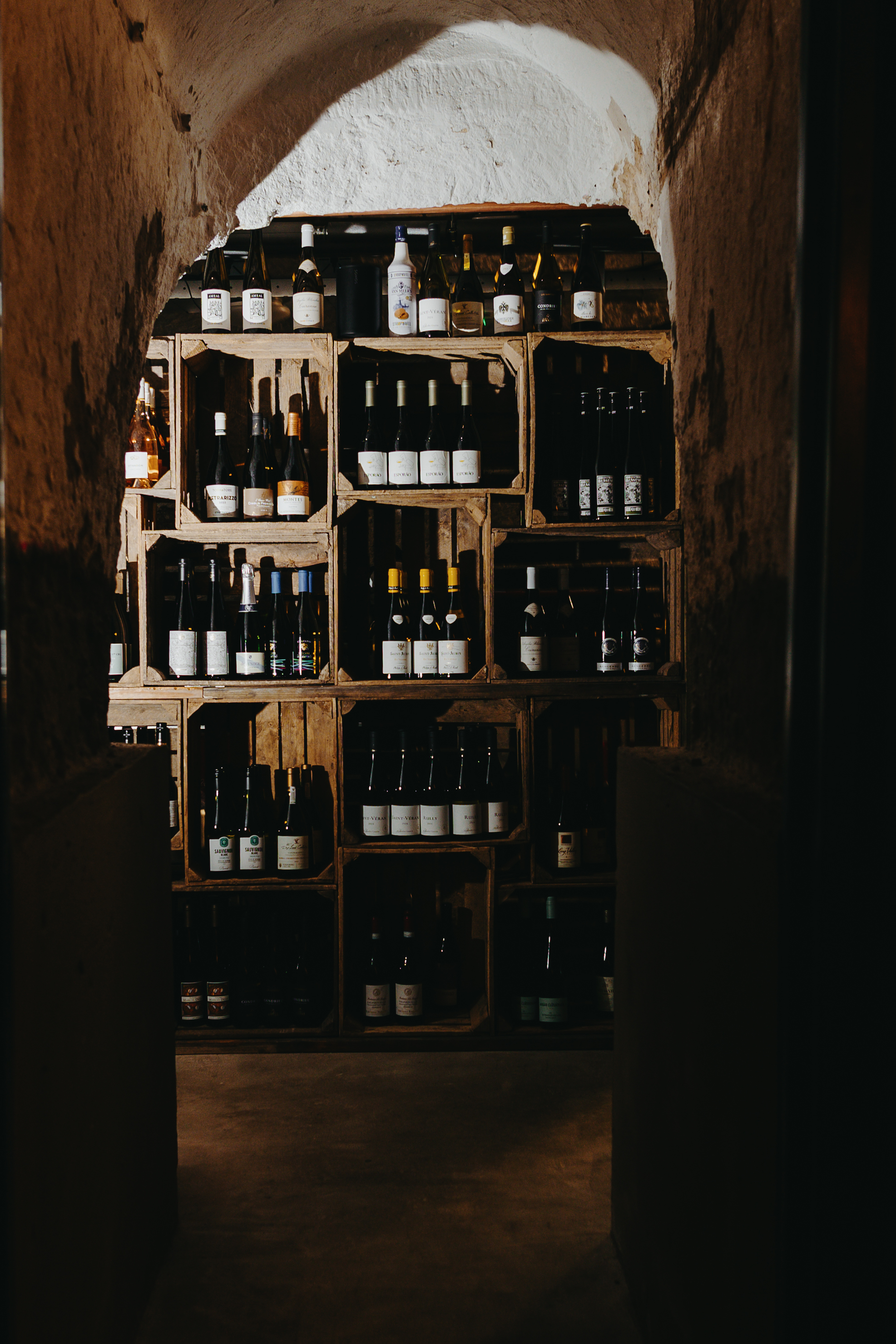 Wijnkelder met houten kisten gevuld met flessen wijn, sfeervol verlicht in een rustieke stenen ruimte.