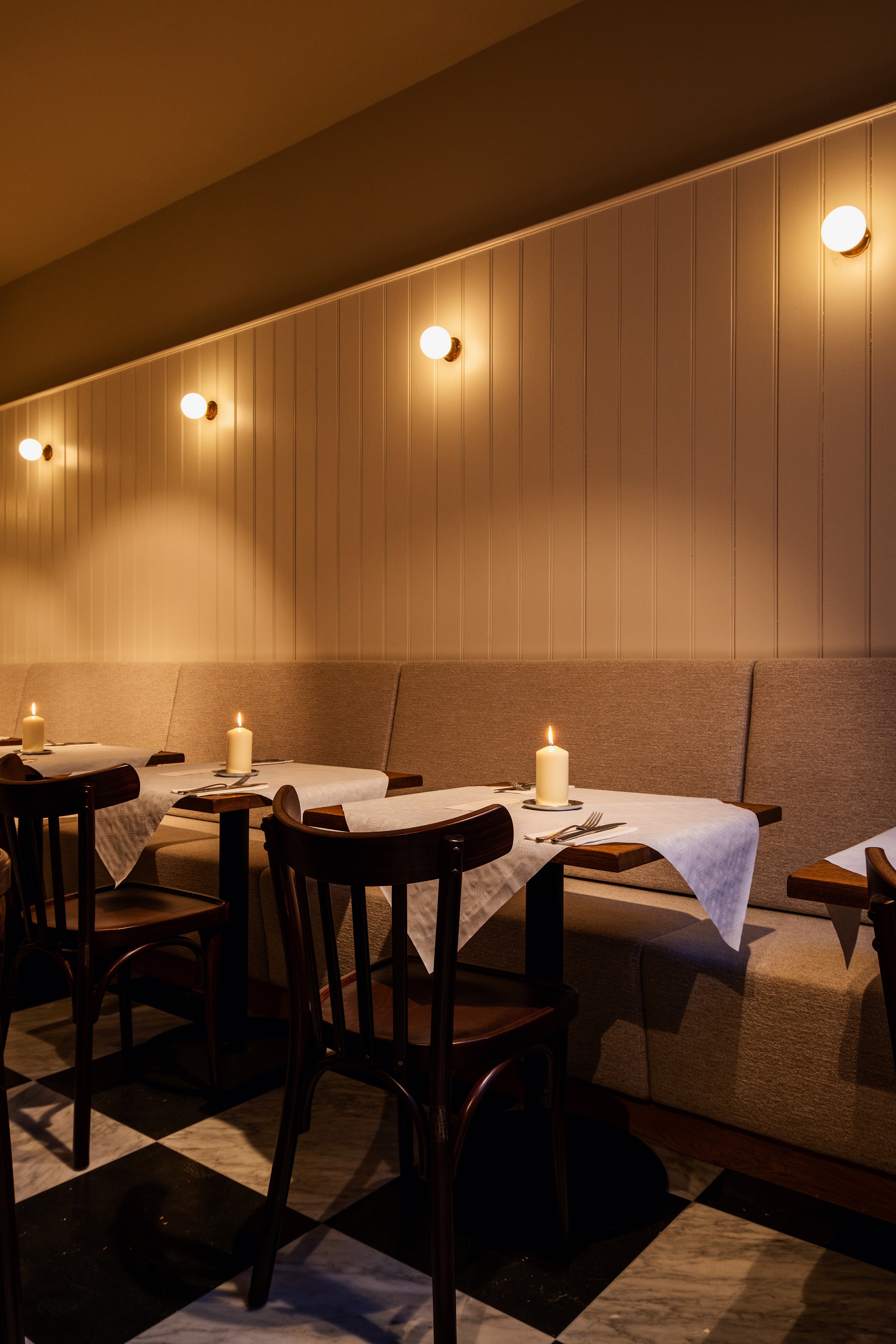 Gezellige eetkamer met houten stoelen, kaarsverlichting op tafels met witte tafellopers en warme wandlampen.