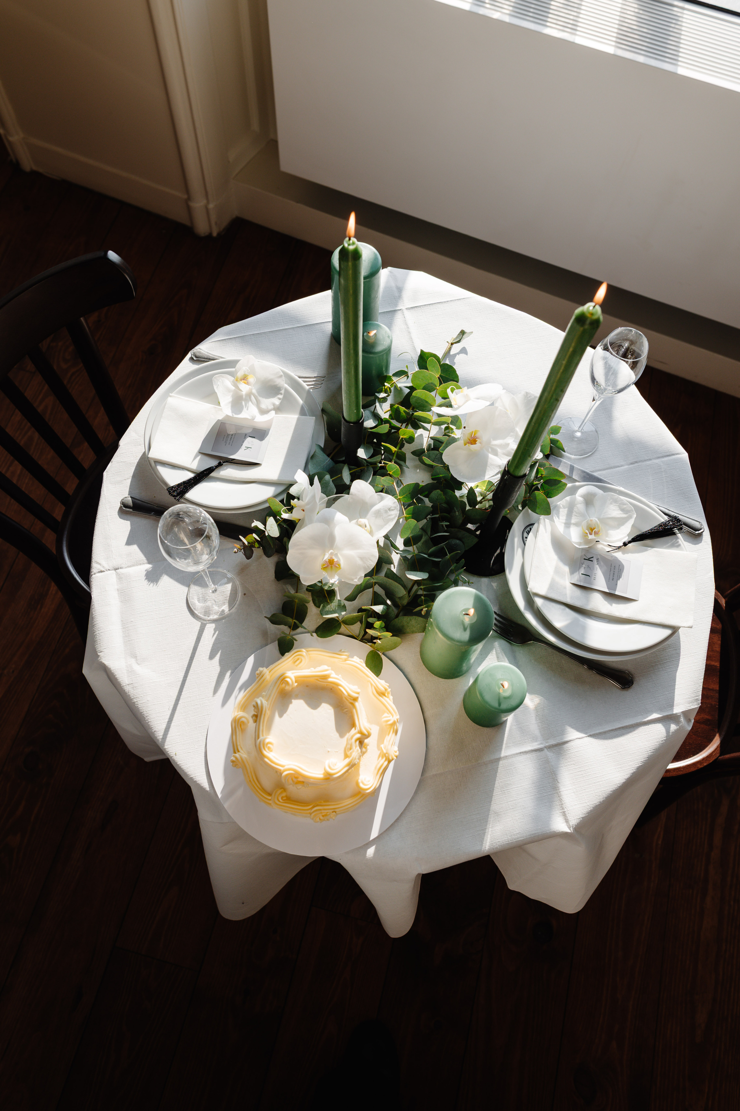 Ronde tafel met witte tafellaken, versierd met groene kaarsen, orchideeën en een kleine witte taart.