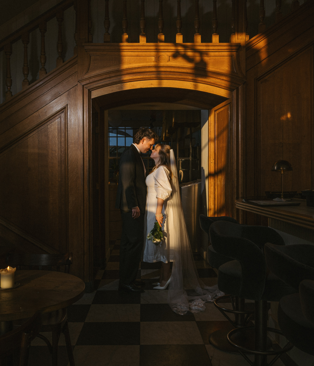 Bruidspaar in zacht zonlicht bij houten trap, romantisch moment in sfeervolle vintage inrichting.