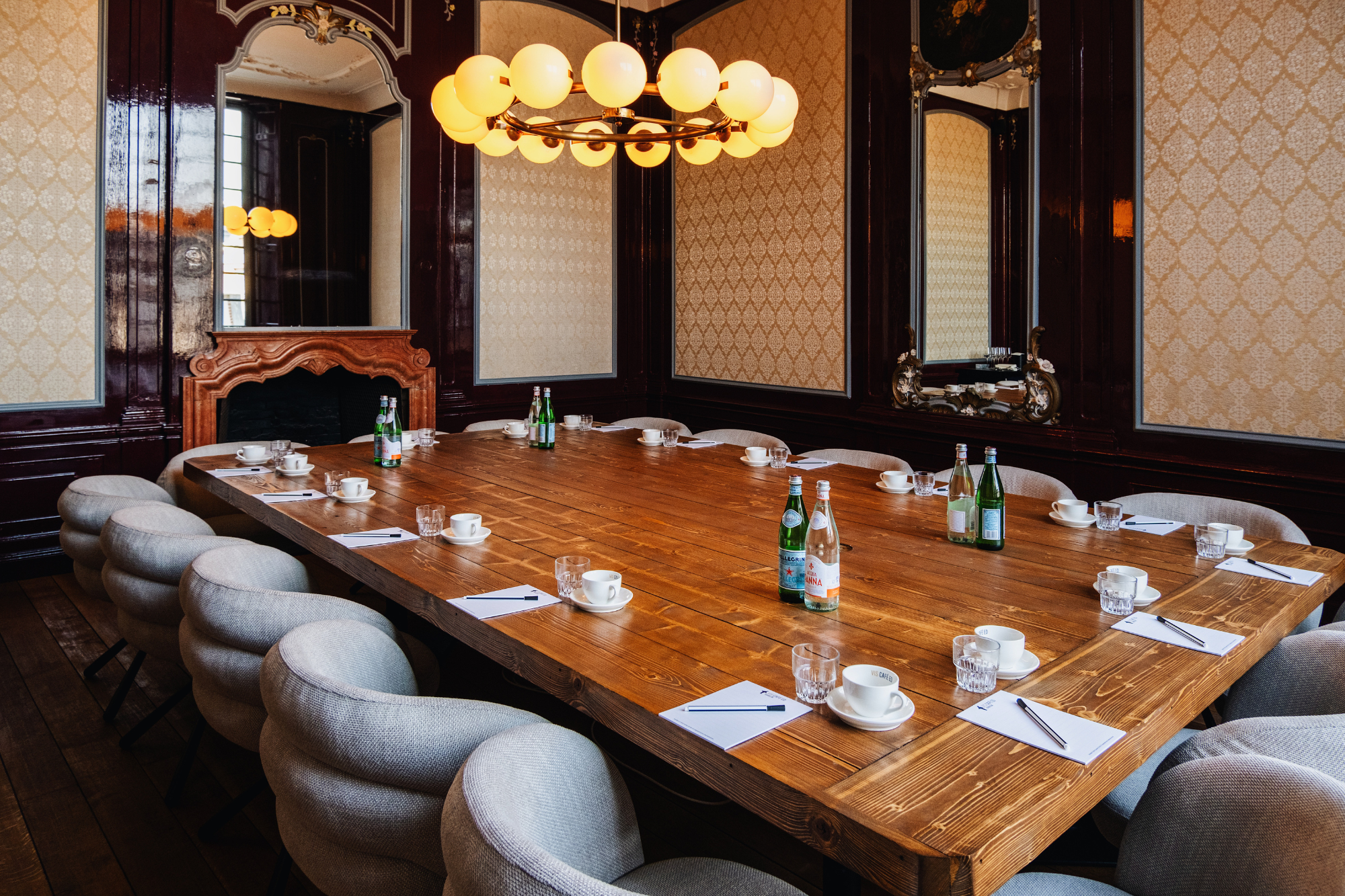 Elegante vergaderruimte met houten tafel, comfortabele stoelen, flessen water, kopjes en notitieblokken.