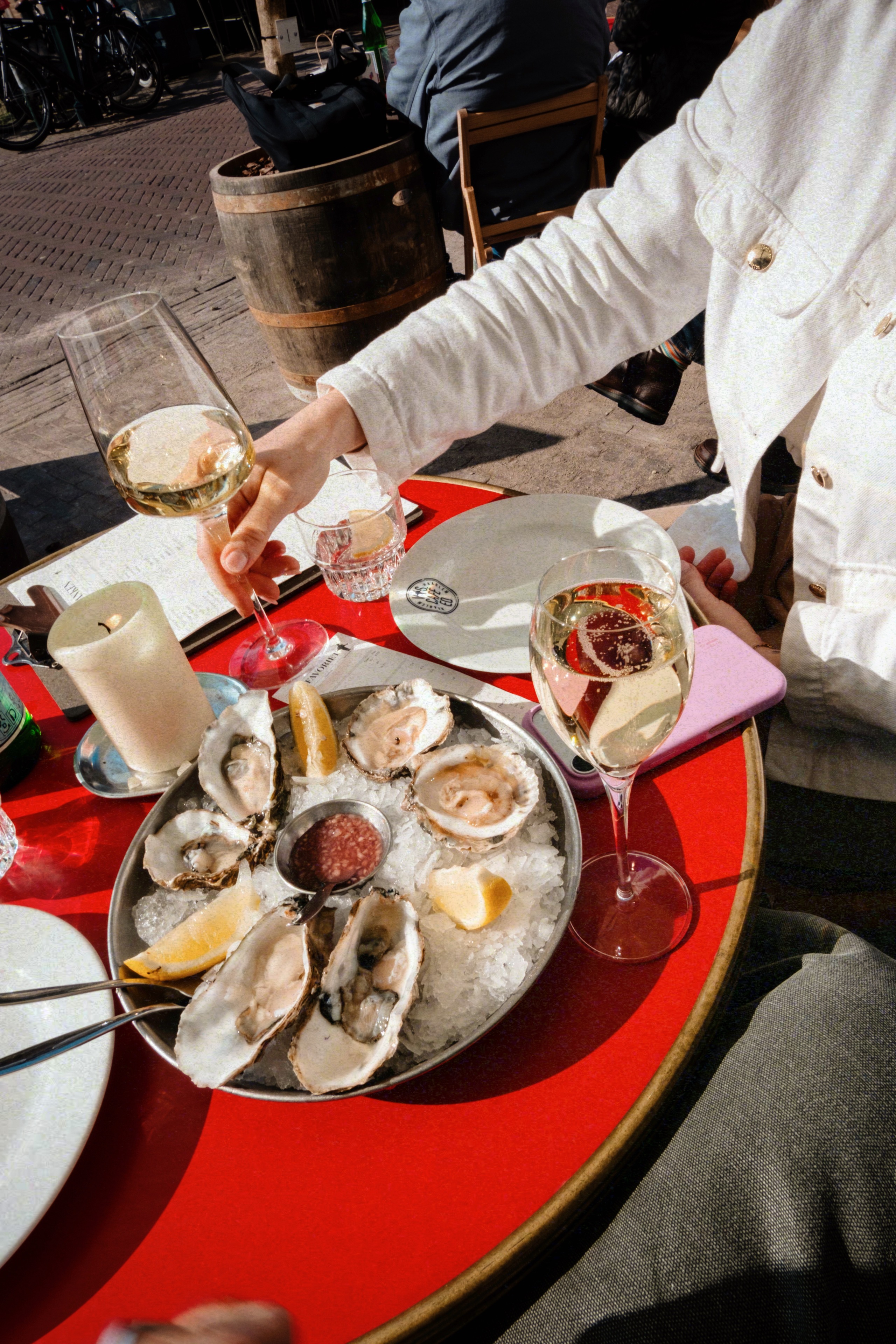 Oesters op ijs met citroen, geserveerd op een rood tafeltje in de zon, vergezeld van glazen witte wijn.