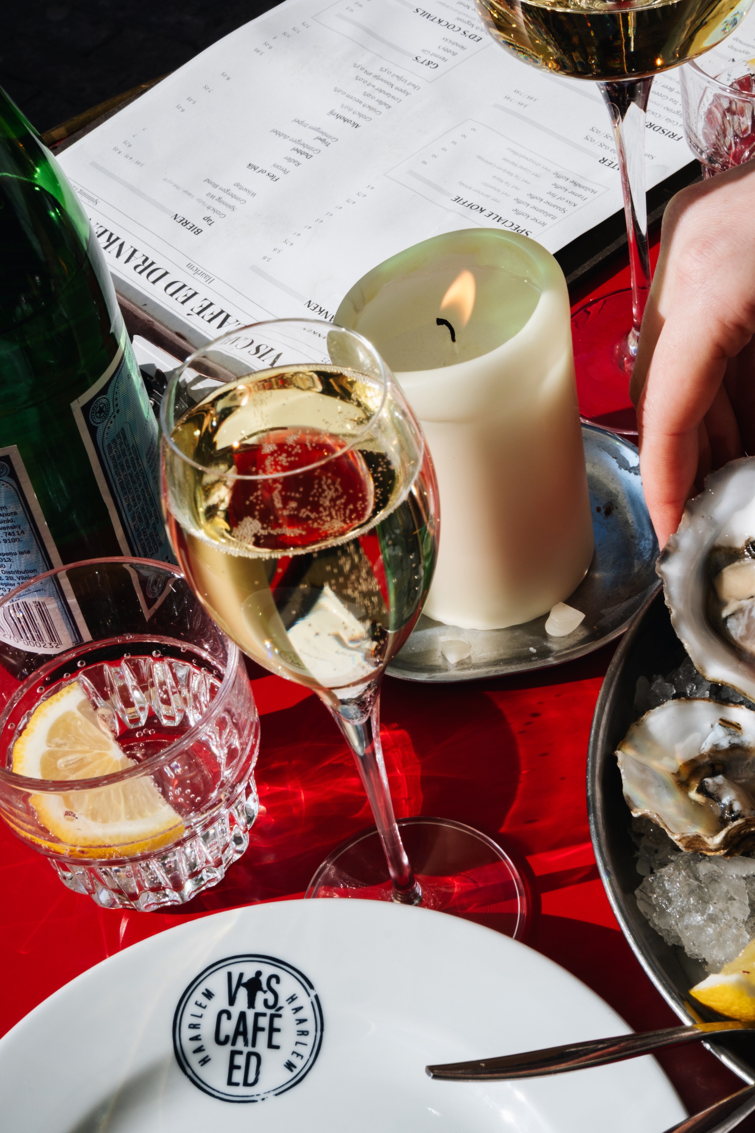 Champagneglas met bubbels, oesters op ijs, brandende kaars en citroen in glas op rood tafellaken.