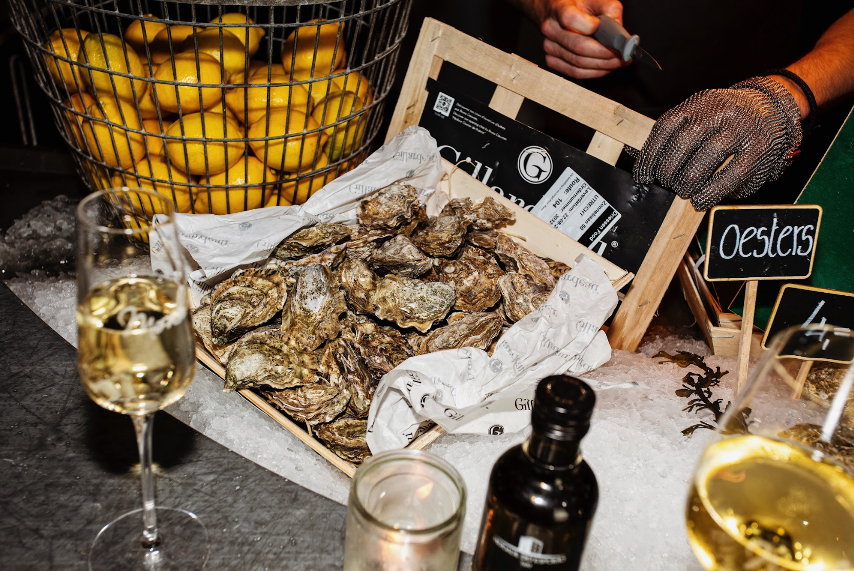 Verse oesters op ijs met citroenen in een mand, een glas witte wijn en een hand met handschoen.