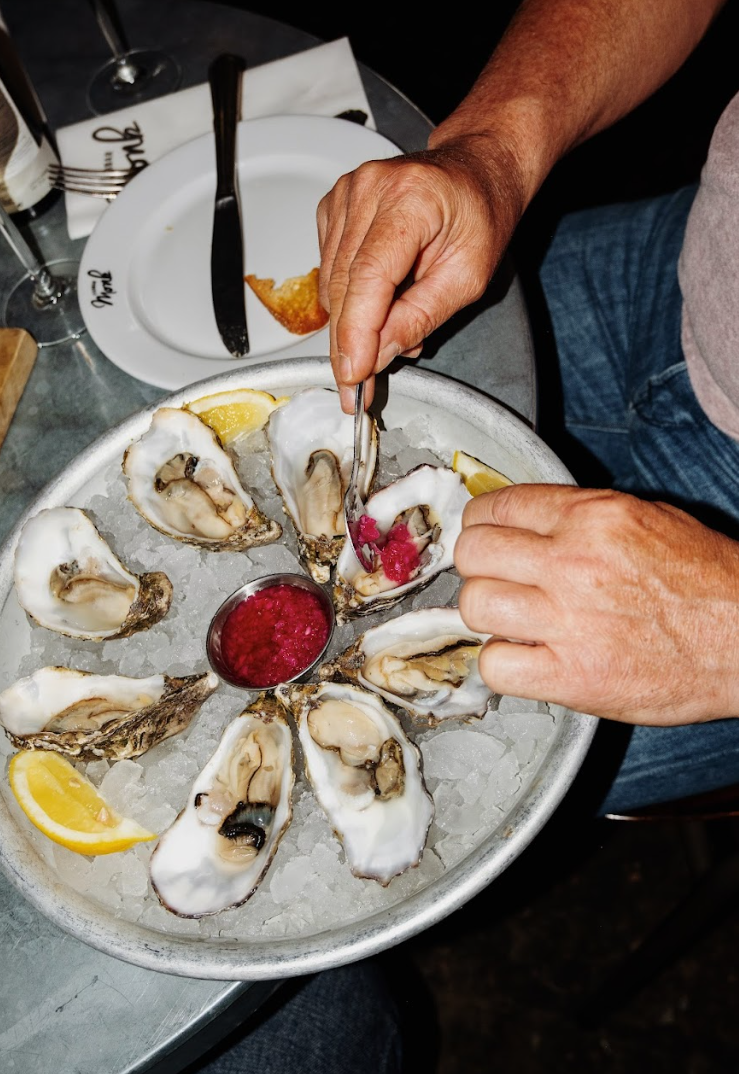 Oesters op ijs met citroenpartjes, gepresenteerd op een metalen schaal, hand voegt rode saus toe.
