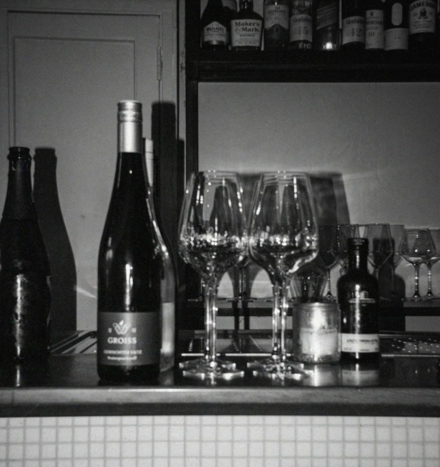 Wijnflessen en glazen op een bar, sfeervol verlicht. Achtergrond met flessen en een kaarsje.