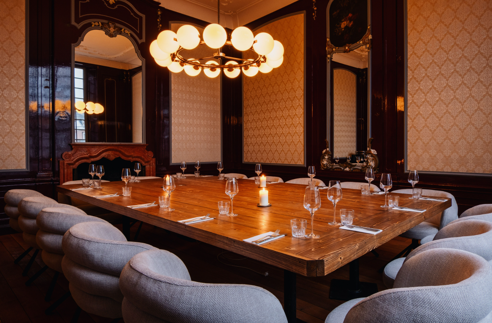 Grote houten tafel met gedekte plekken in een elegante kamer, sfeervol verlicht door een kroonluchter.