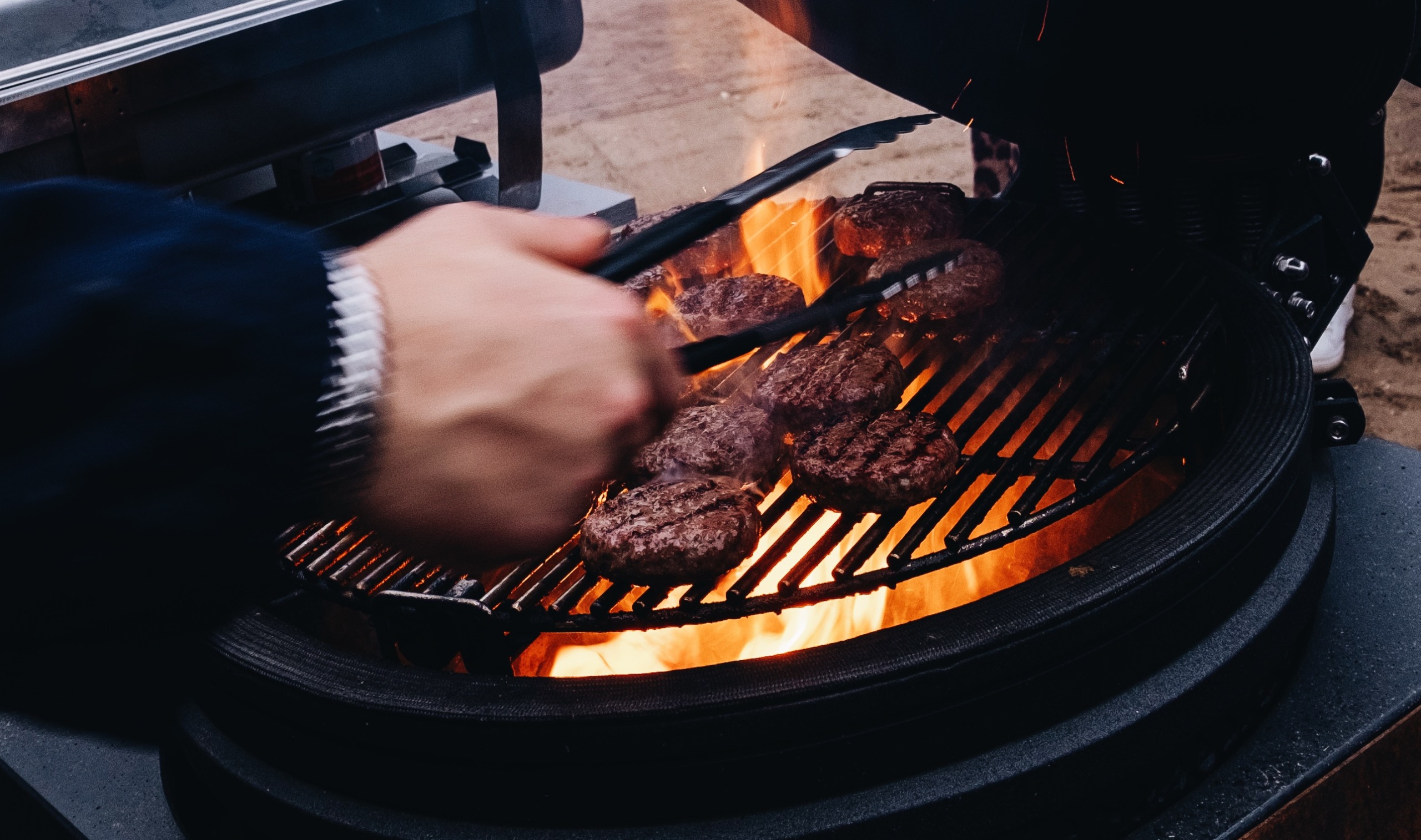 Hamburgers sissen op een hete barbecue met vlammen, hand draait burgers om met een tang.