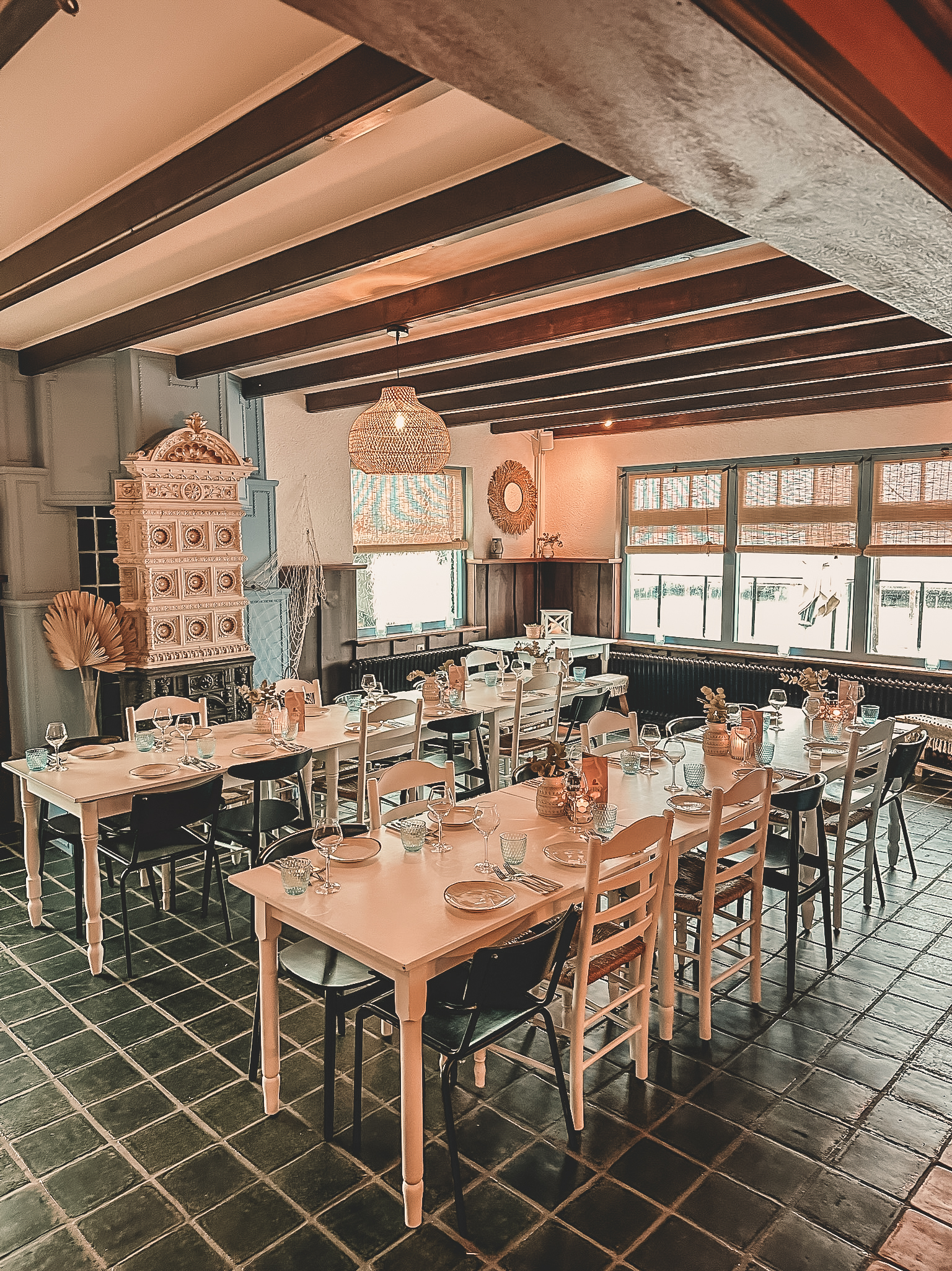 Gezellige eetzaal met houten balken, gedekte tafels, witte stoelen en warme verlichting, landelijke sfeer.