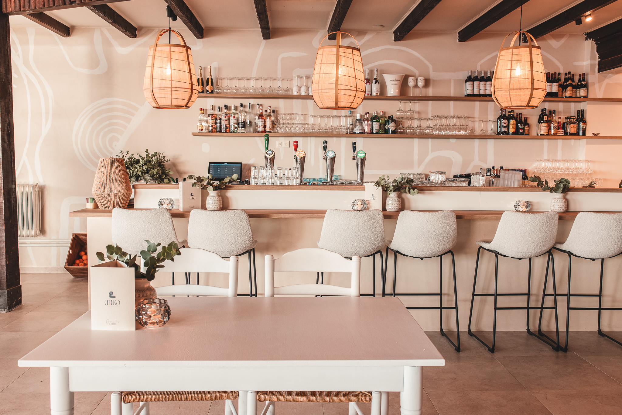 Lichte, moderne bar met houten balken, zachte stoelen, hanglampen en een uitnodigende sfeer.