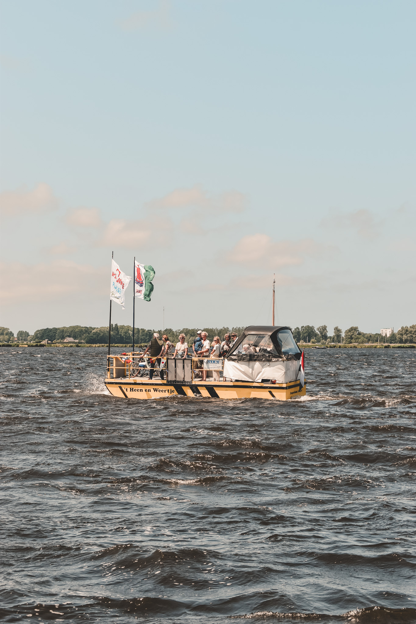 Boot met passagiers op een zonnig meer, omringd door groen landschap en blauwe lucht.