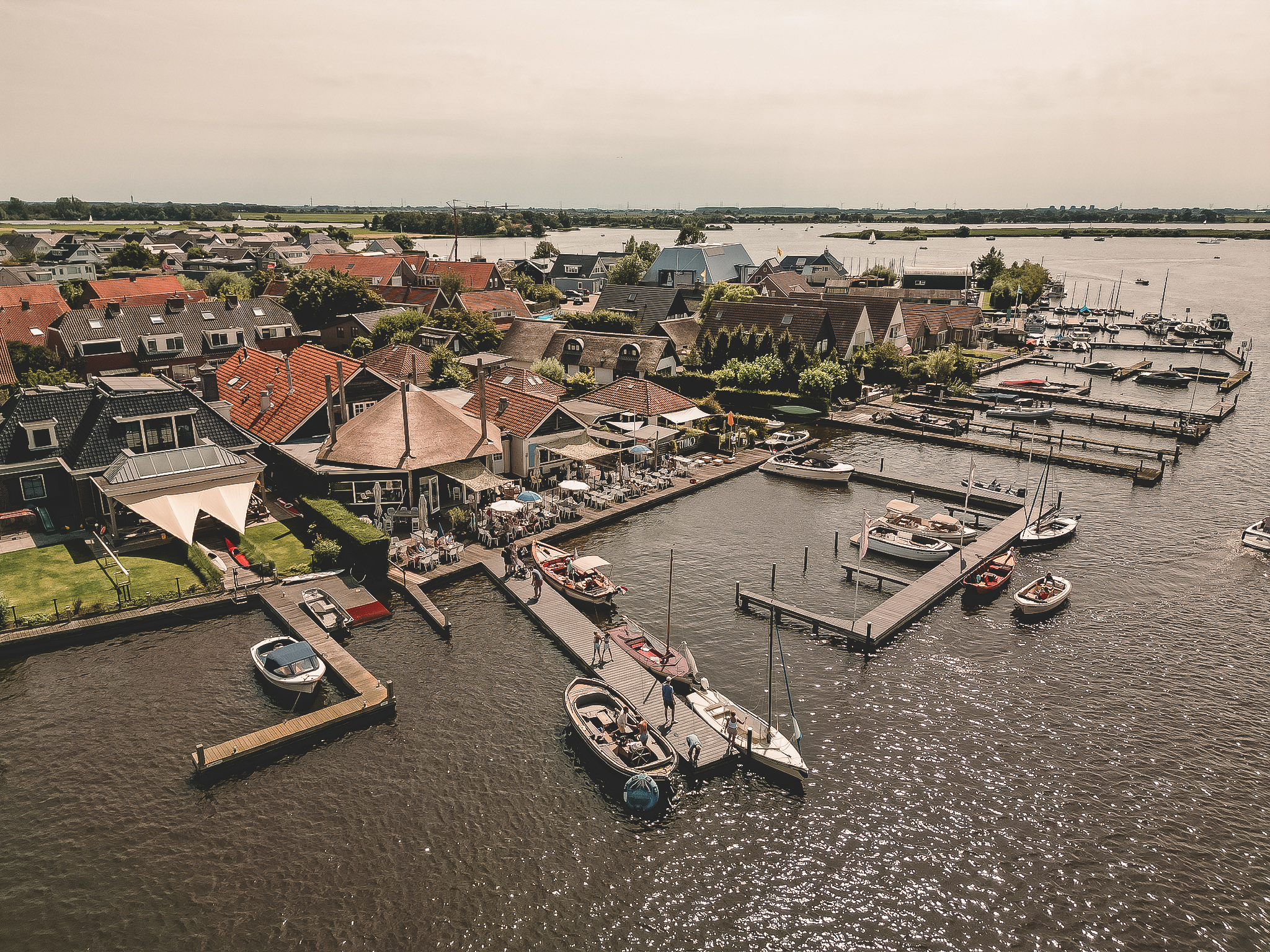 Luchtfoto van een pittoresk dorp aan het water met jachthaven, boten en terrassen onder een bewolkte hemel.