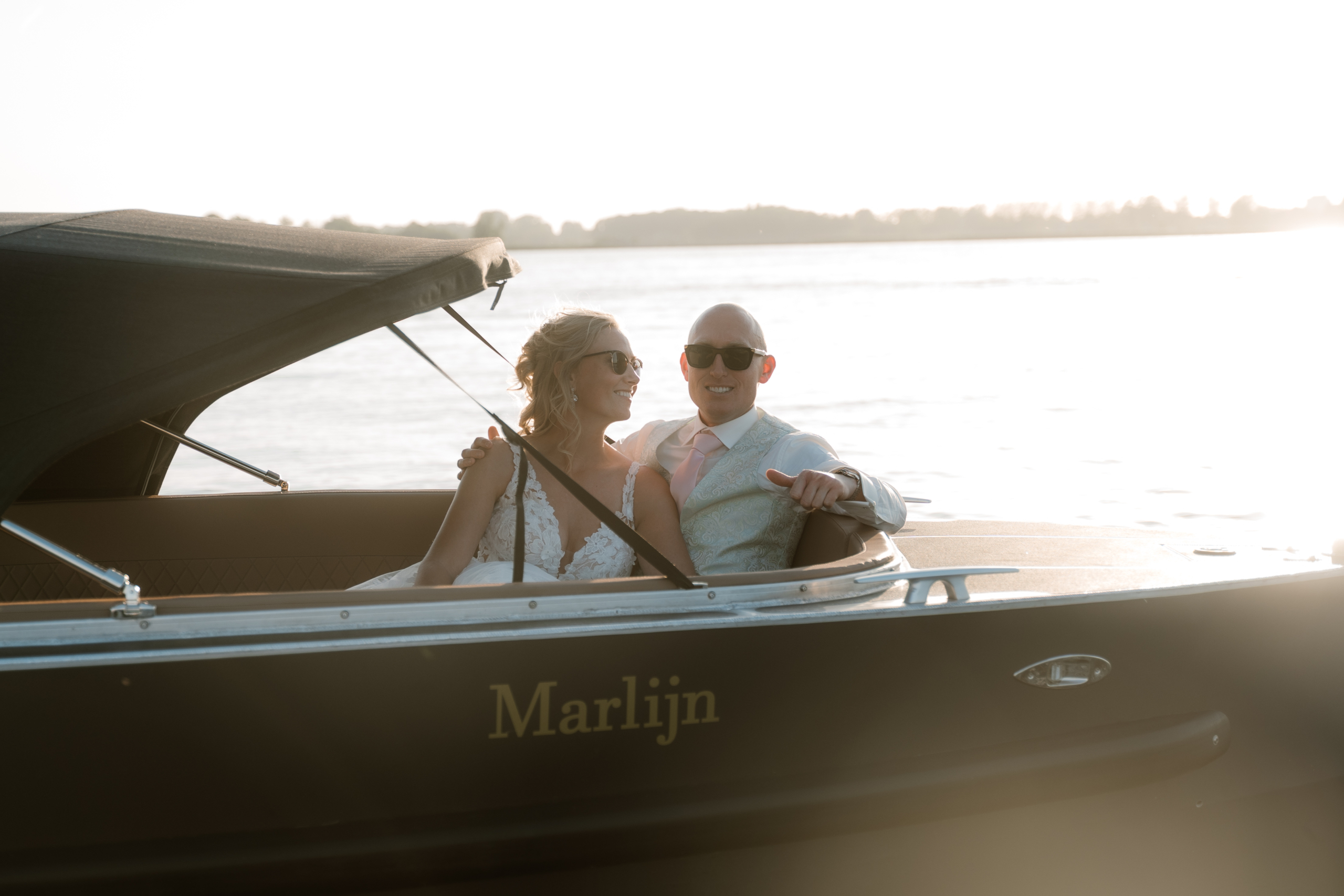 Stel in een speedboot op het water, een lachend paar in bruiloftskleding geniet van de zonsondergang.