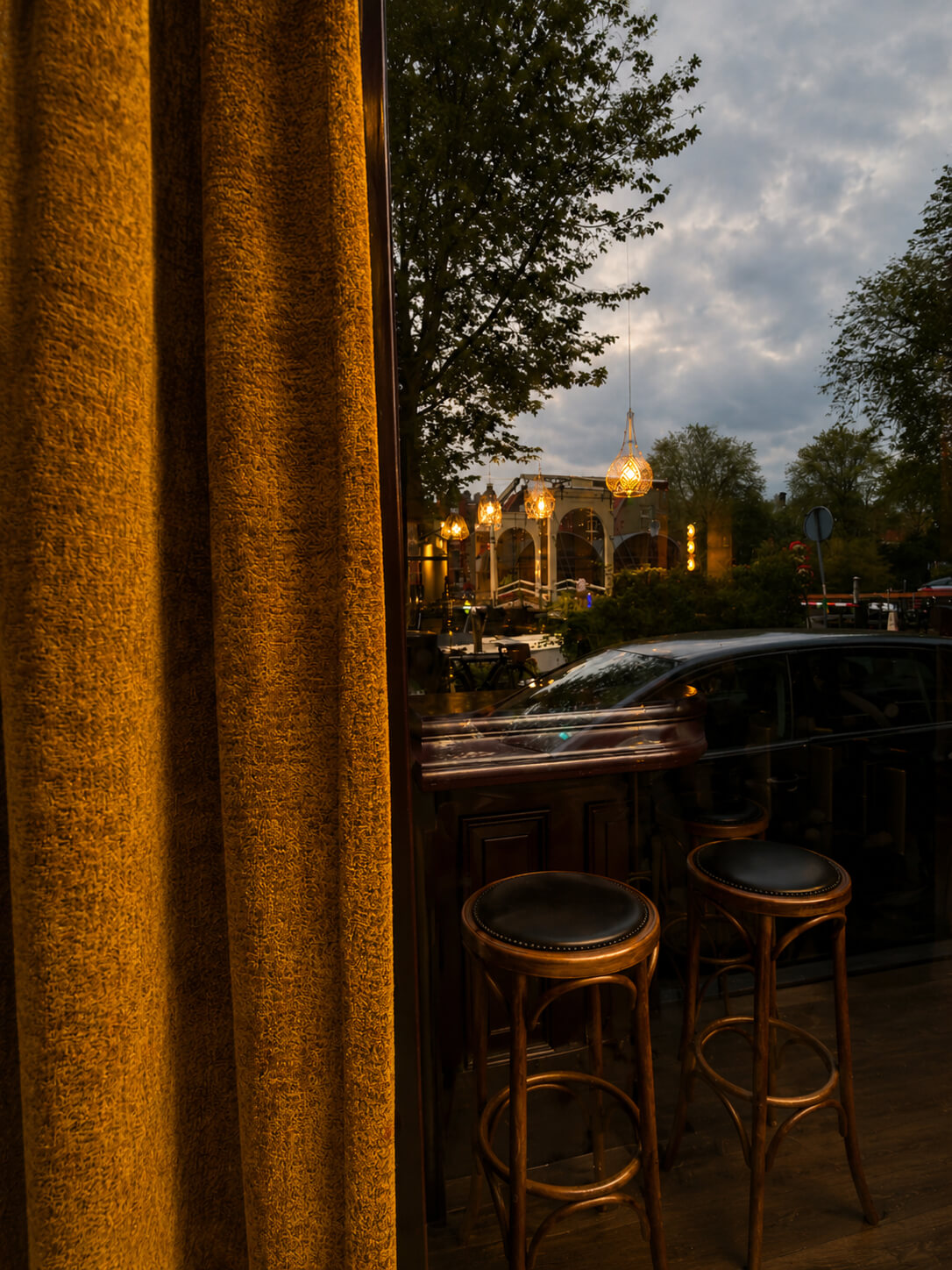 Gezellige barhoek met houten barkrukken, warme bruine gordijnen en sfeerverlichting bij zonsondergang.