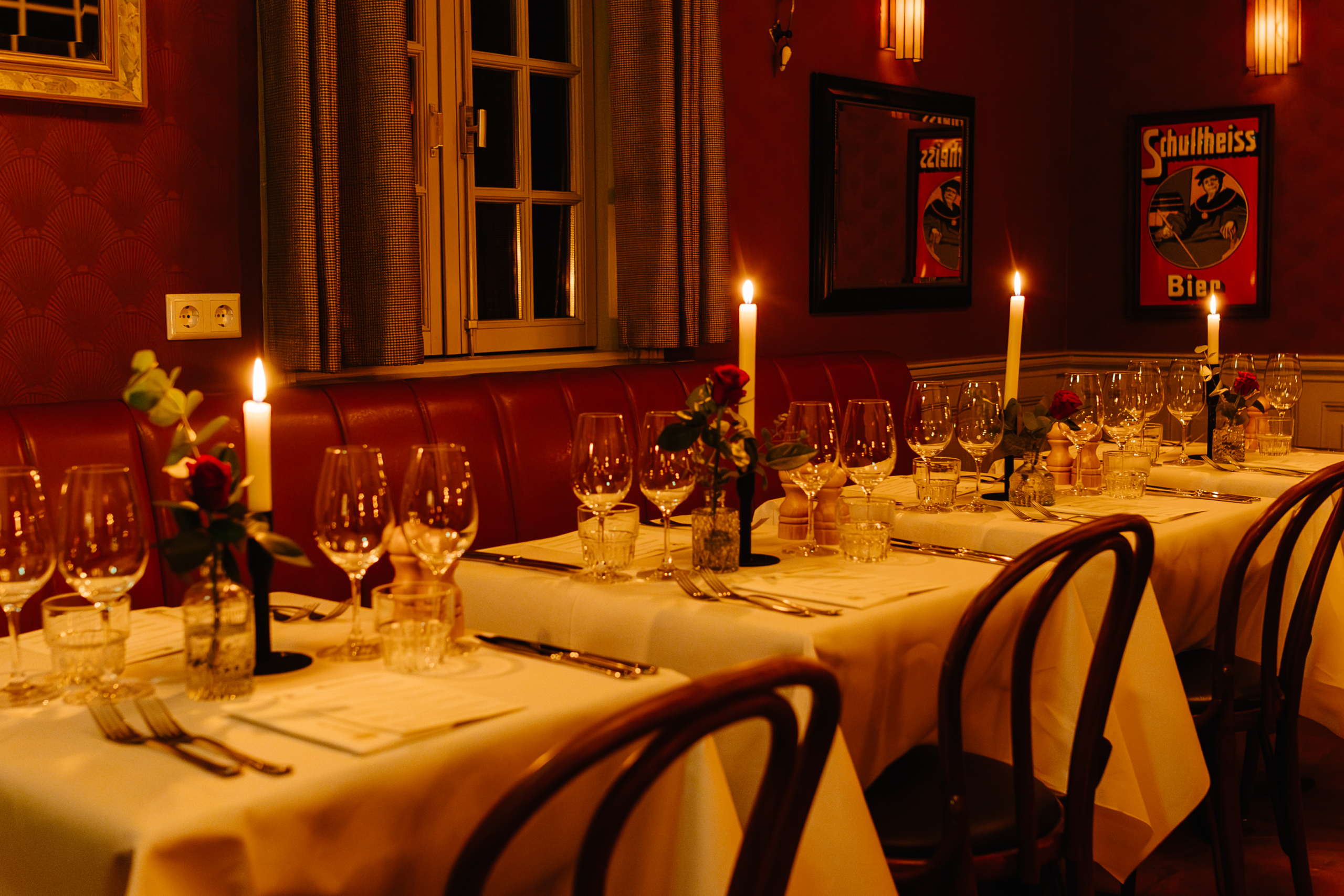 Gezellige restaurantsetting met kaarsverlichte tafels, rode leren banken en gedekte tafels met wijnglazen.