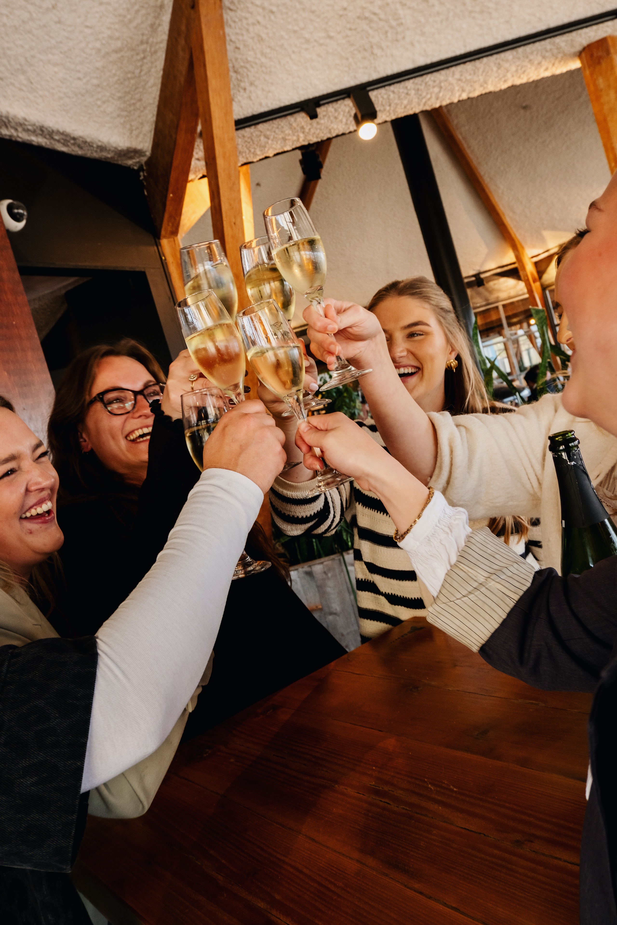 Vrolijke groep vrienden proost met glazen champagne in een gezellige, warme restaurantomgeving.
