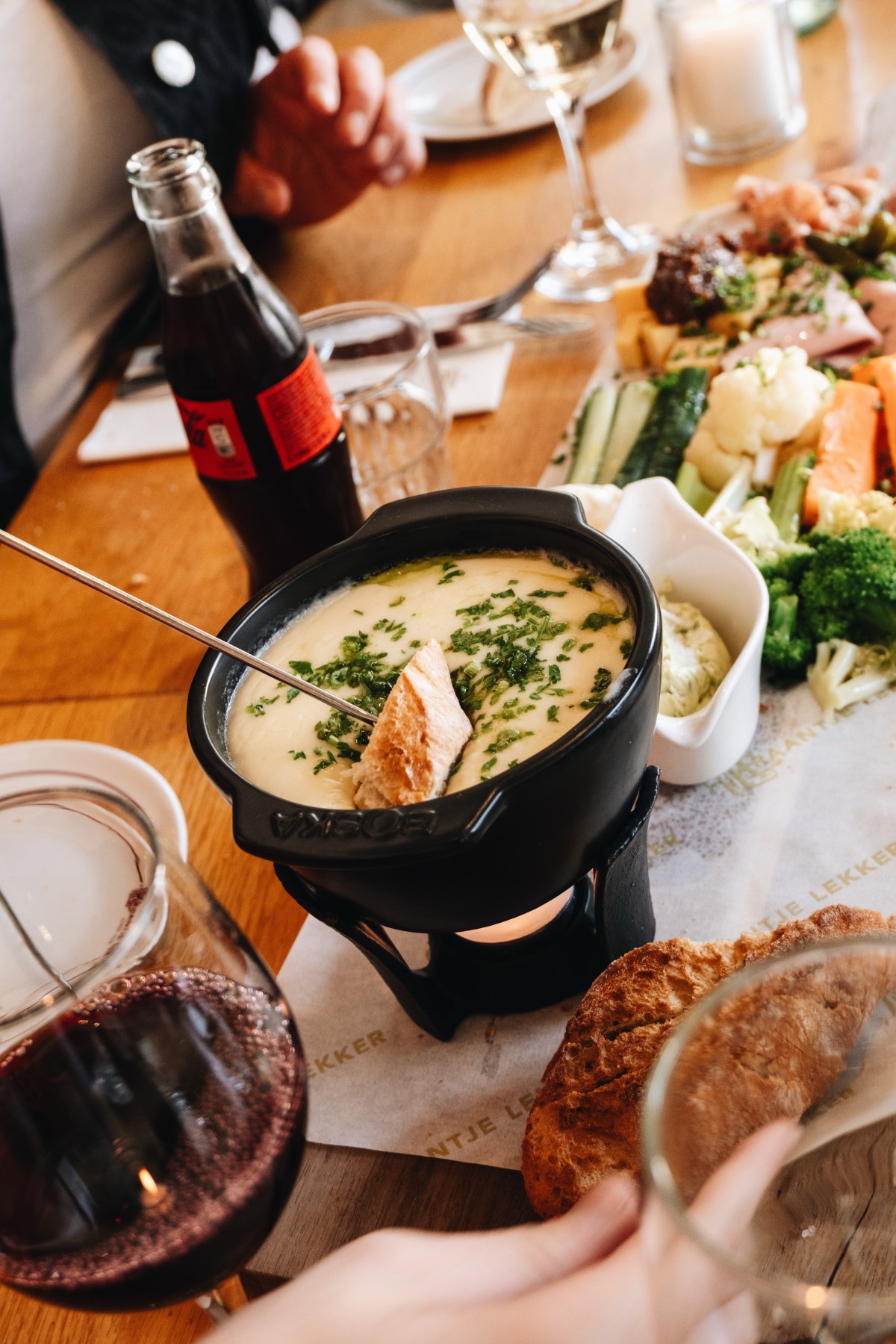 Gezellig tafereel met kaasfondue, verse groenten, brood en rode wijn op houten tafel, warme sfeer.