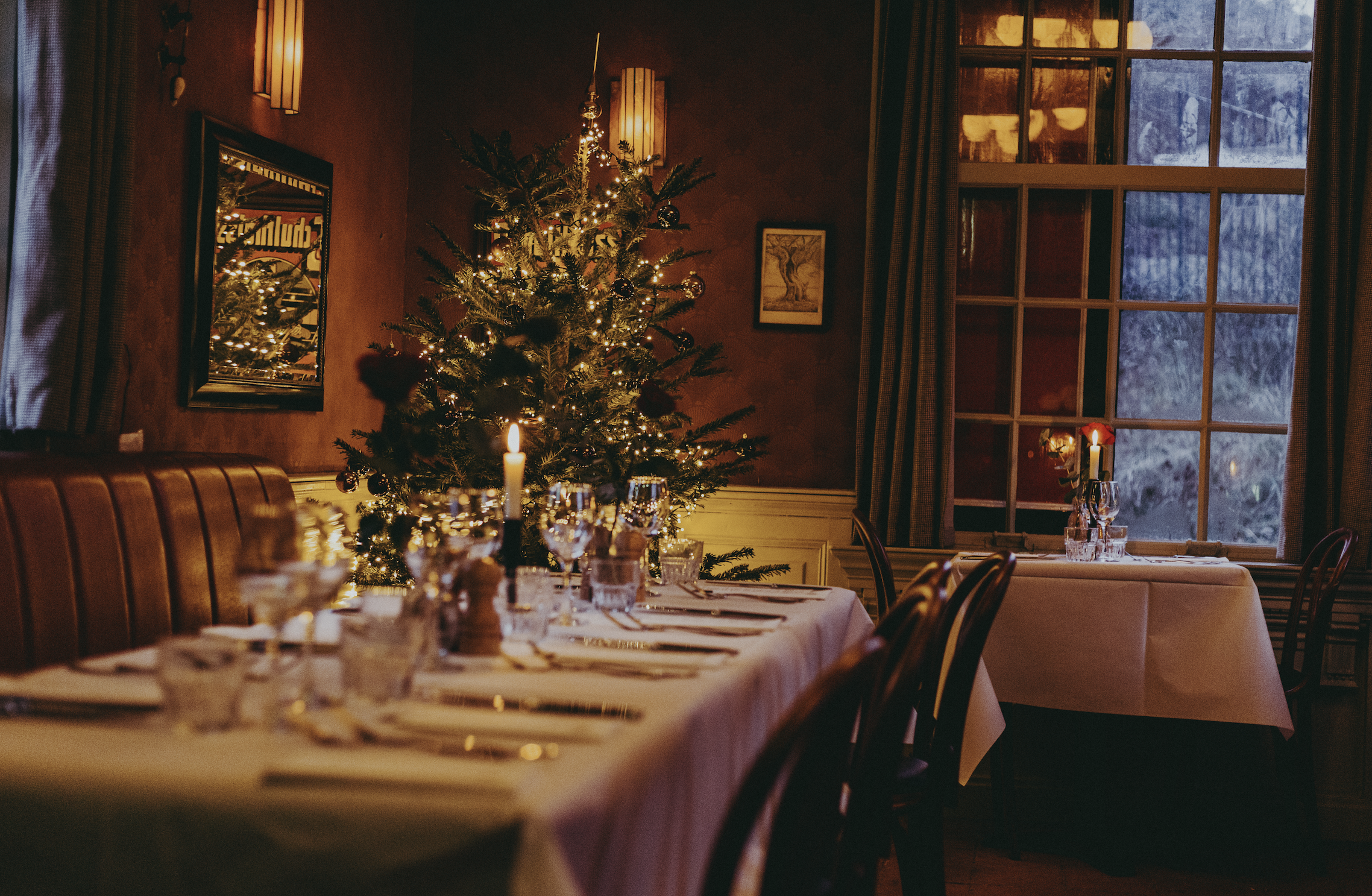 Gezellige restaurantsetting met kerstboom, gedekte tafels, kaarslicht en warme bruine tinten.