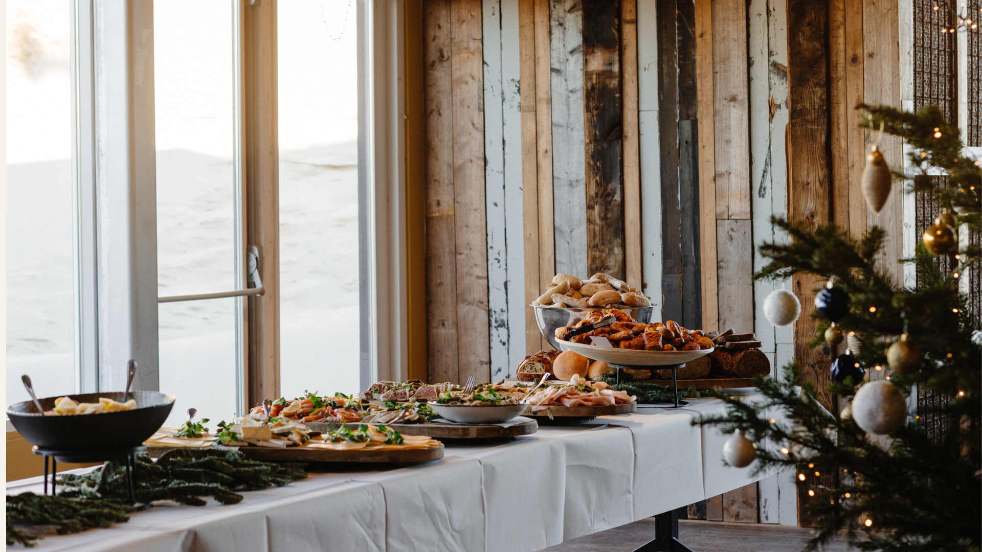 Buffettafel met diverse broodjes, vleeswaren en salades in een rustieke ruimte met houten muren en kerstdecoratie.