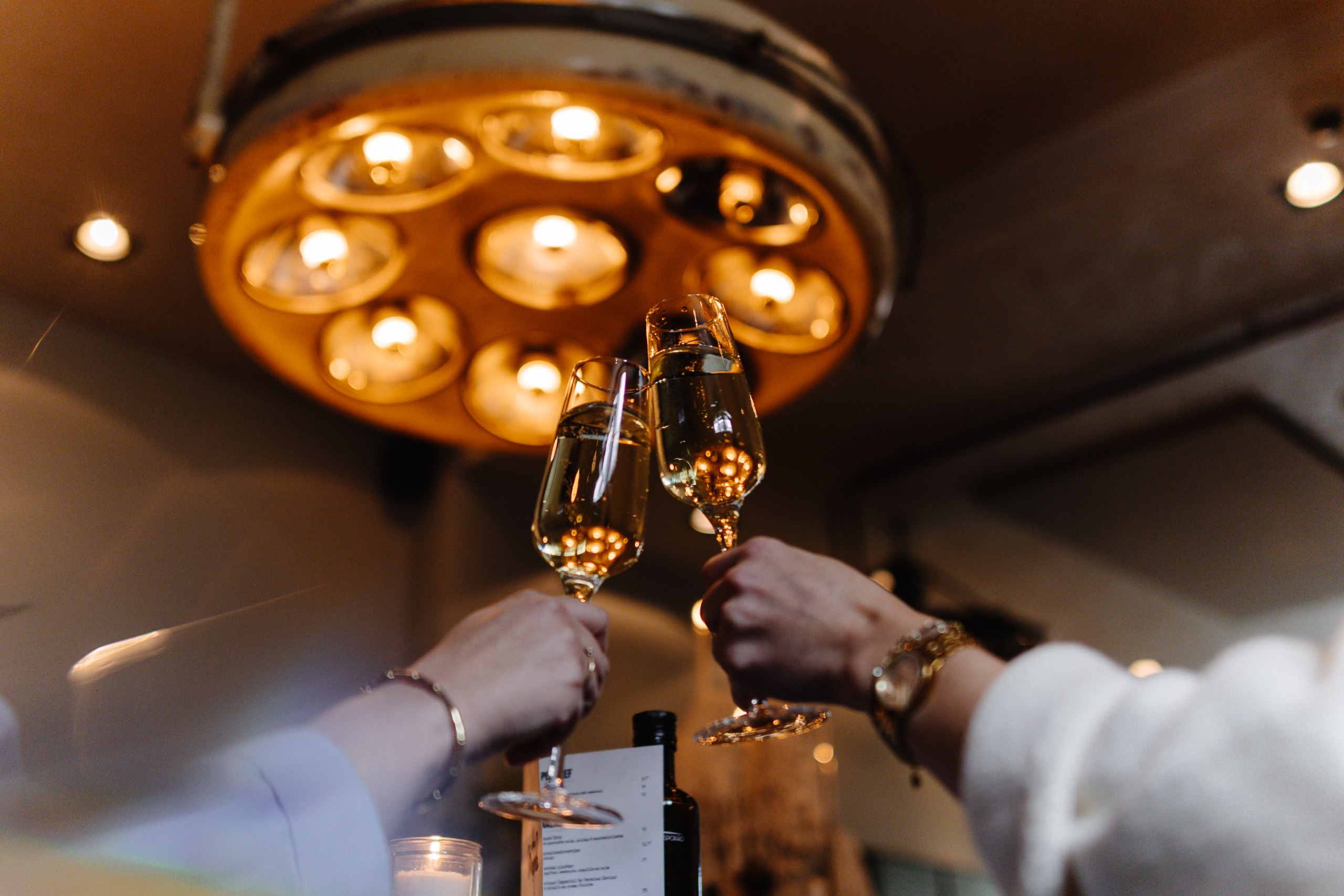 Twee handen klinken met champagneglazen onder warme, sfeervolle verlichting in een gezellige setting.