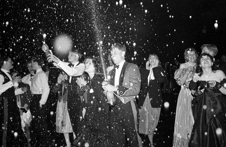 Feestelijke menigte in avondkleding viert met champagne, bruisende sfeer en lachende gezichten.